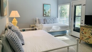 A bedroom with two beds, a nightstand, a lamp, a painting, a dresser, and a door leading outside. - Sleeps 9! Serene Sea Palms Golf Condo on St Simons|Close to Beach, Restaurants!  (St. Simons Island)