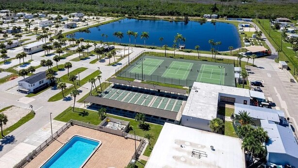 Eine Vogelperspektive zeigt einen Urlaubsort mit mehreren Tennisplätzen, einem großen zentralen Pool und verschiedenen Villen.