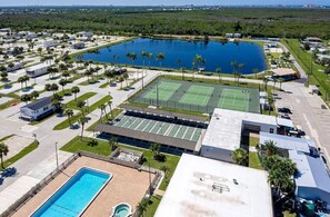 Vista aérea de un resort con varias canchas de tenis, una amplia piscina central y varias villas.