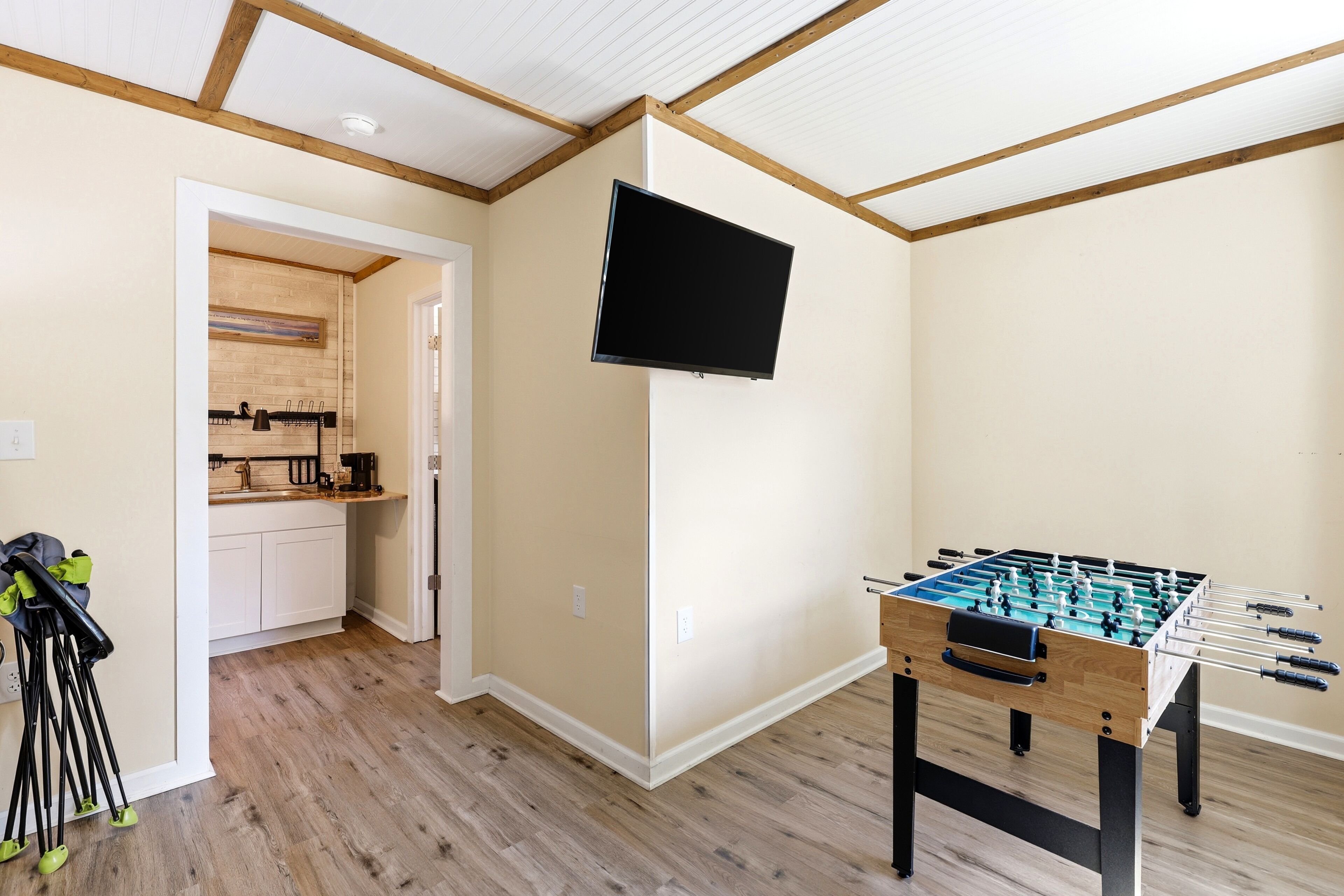 Una habitación con mesa de fútbol de mesa, televisor montado en la pared y cocina visible a través de una puerta abierta.