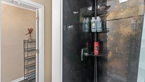 Un bagno con box doccia in vetro, una mensola in metallo con articoli da toilette e una porta che dà su un'altra stanza.