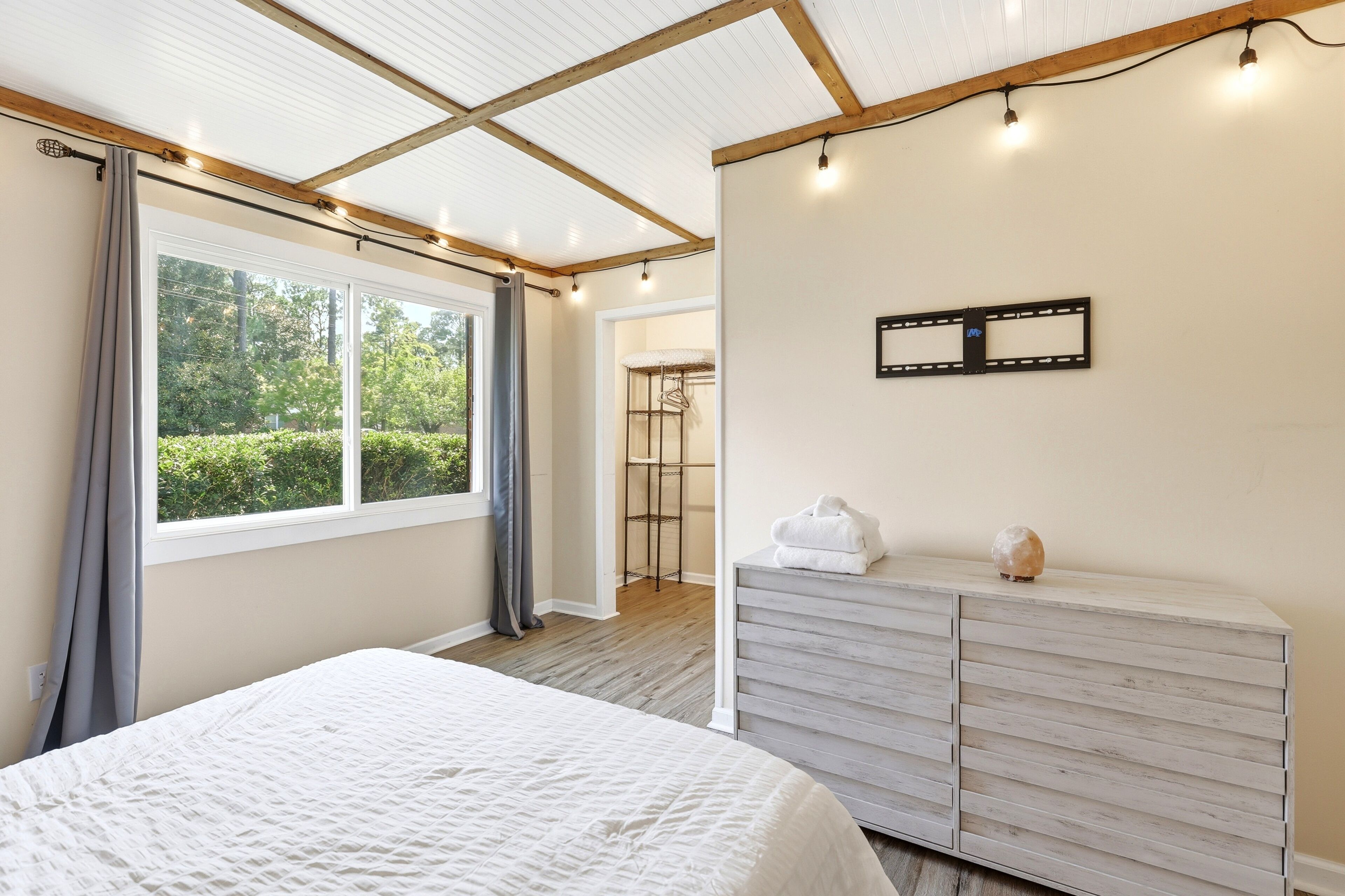 A bedroom with a bed, a dresser, a mirror, and a window with curtains.