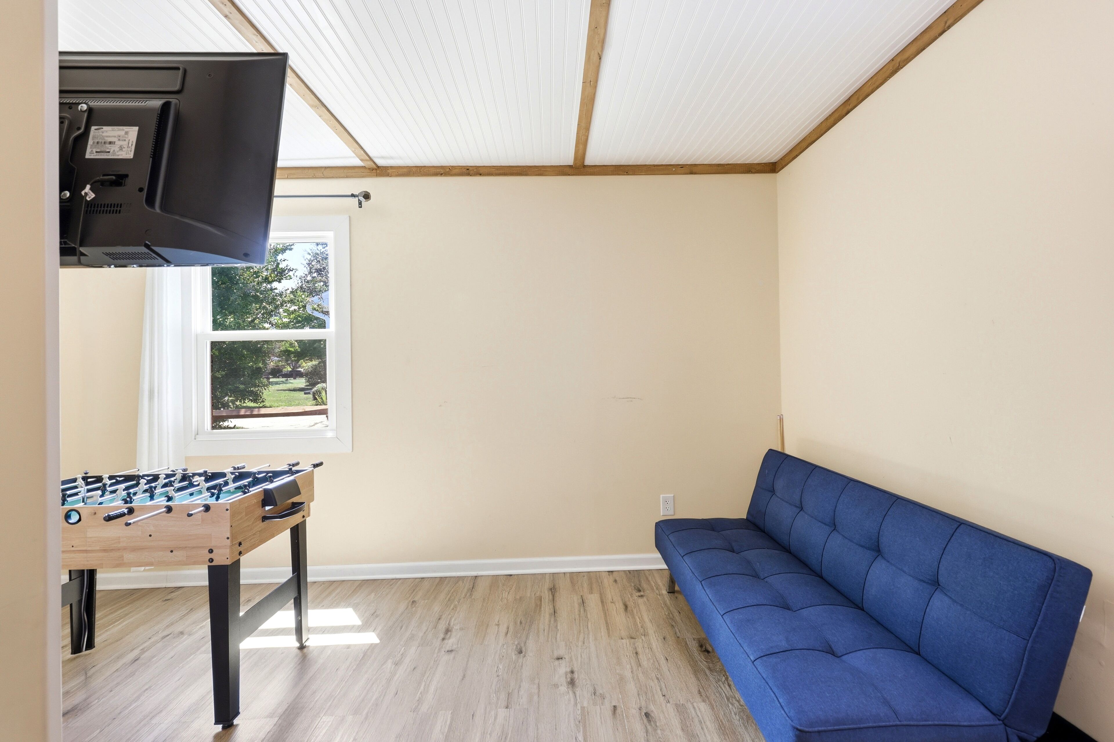 A room with a foosball table, a blue sofa, and a television on a stand.