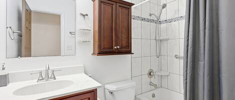 A bathroom with a wooden vanity, a toilet, a bathtub, and a shower.