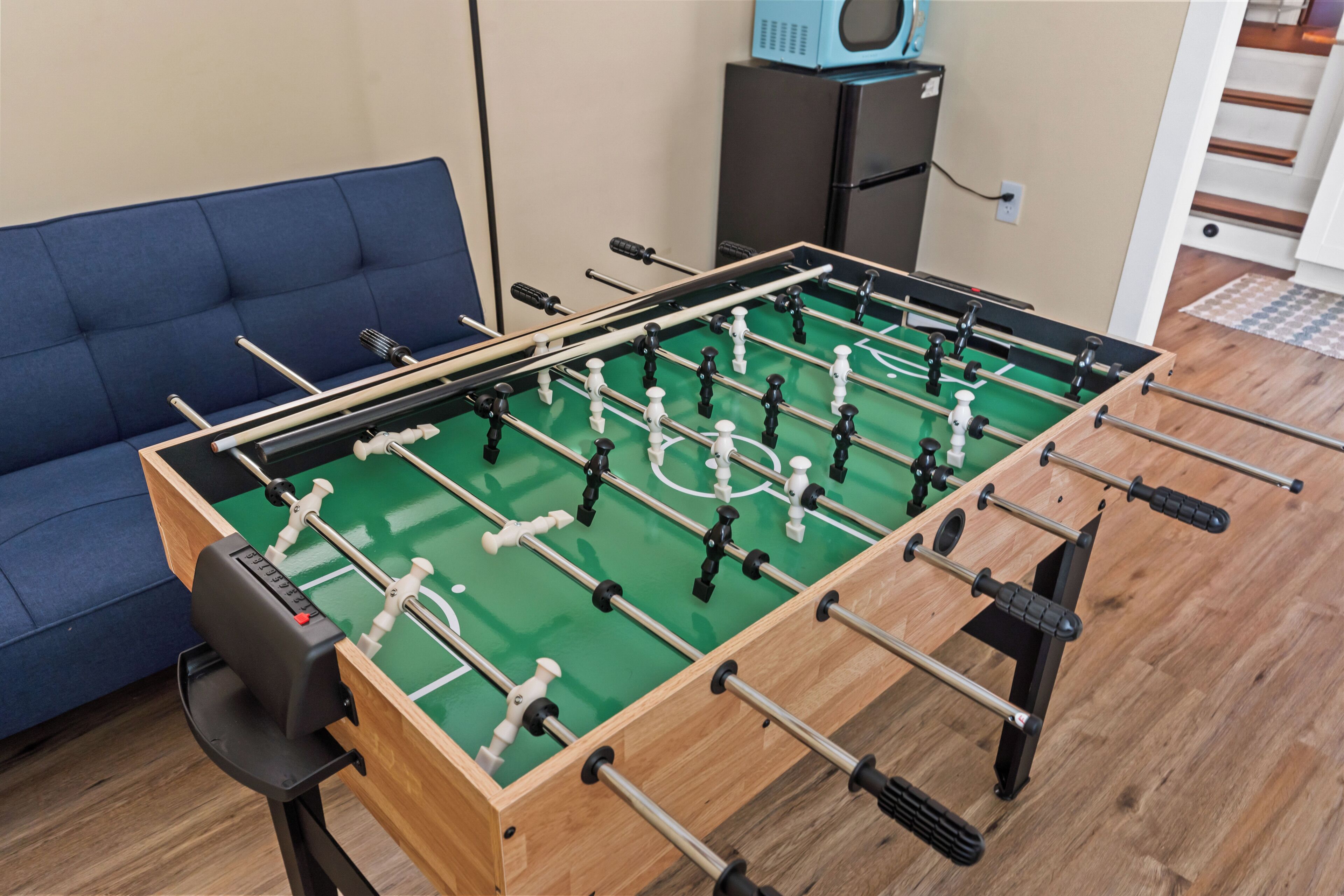 A foosball table in a room with a blue sofa and a small black cabinet.