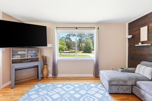 A living room with a flat-screen TV, a sofa, a coffee table, and a window with curtains.