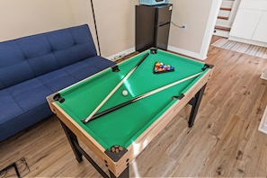 A pool table with a blue sofa and a refrigerator in the background. - Family Beach Retreat; Hot Tub, Private Yard and Game Room (Kings Grant)