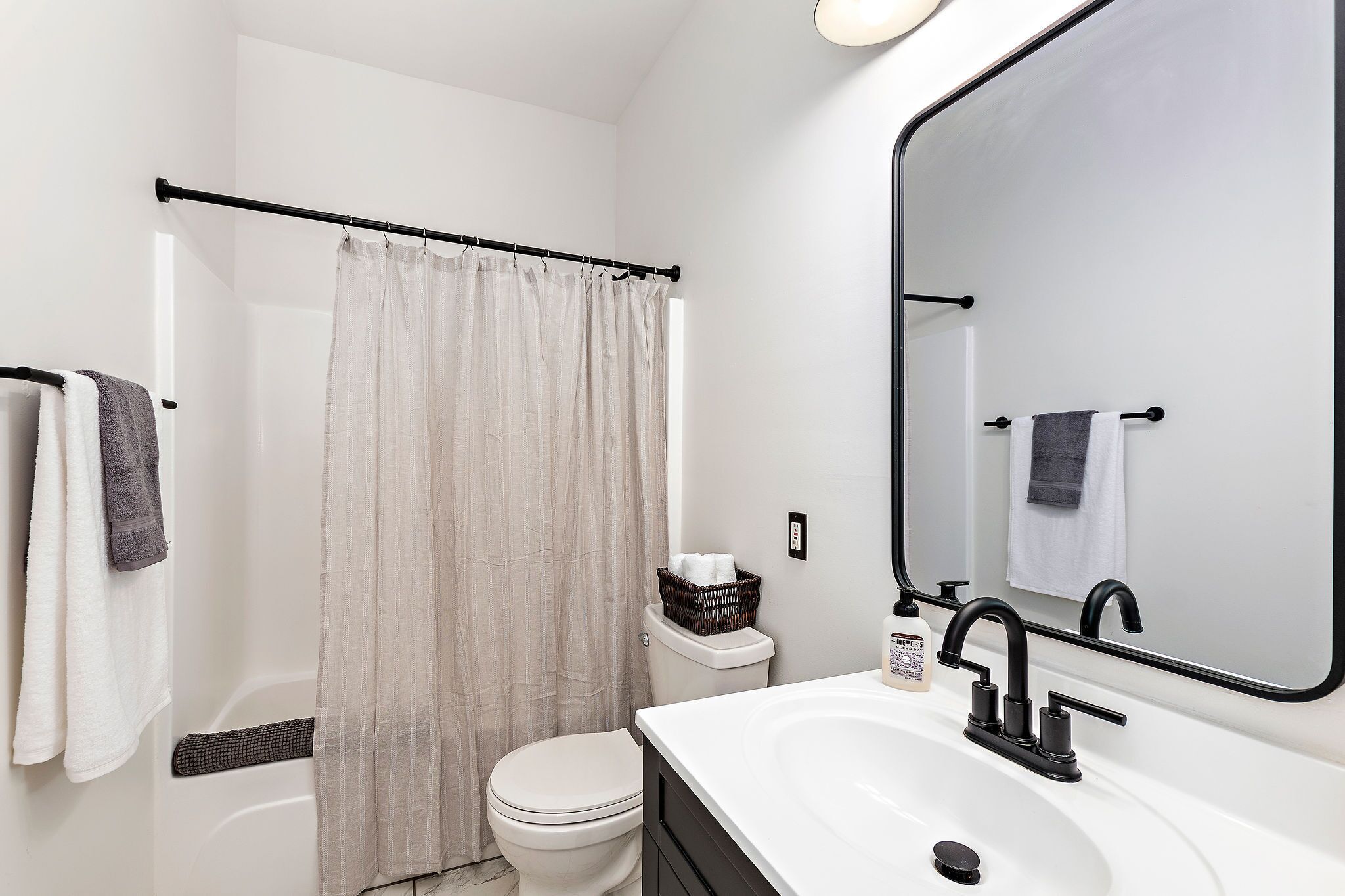 A modern bathroom with a white toilet, a black bathtub, a white sink with a black faucet, and a large mirror.