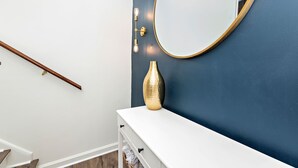 Ein Badezimmer mit weißem Waschtisch, einer goldenen Vase und einem runden Spiegel an einer dunkelblauen Wand.