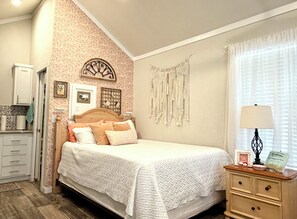 A bedroom with a bed, a nightstand, a wall-mounted macrame, and a framed picture. - Poppy Seed Cottage (Canyon Lake)