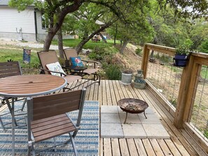 Une terrasse en bois avec une table ronde et des chaises, un foyer et des plantes en pot.
