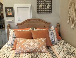 Un lit avec une literie à motifs et plusieurs oreillers, une tête de lit en bois, une porte blanche et un élément décoratif fixé au mur.