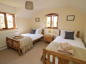 A bedroom with two beds, a bedside table with a lamp, and a window with curtains. - Ellenhall Farm Cottage (Stafford)