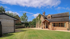 Un grand jardin à l’arrière de la maison, avec une pelouse bien entretenue, une terrasse en bois et une maison en briques dotée de grandes fenêtres et d’une cheminée.