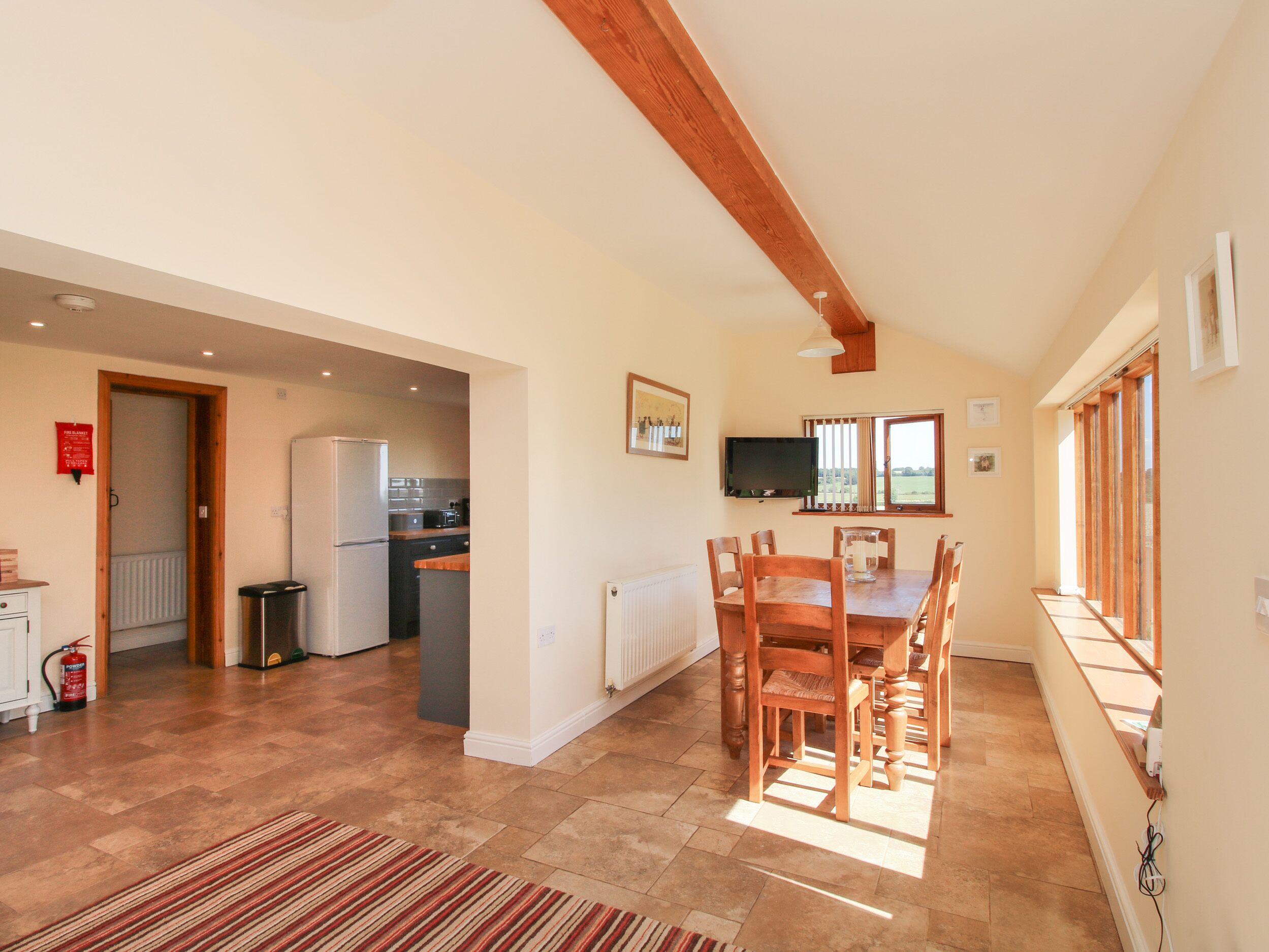 A spacious kitchen with a refrigerator, stove, and wooden cabinets. There is a dining area with a table and chairs, and a window providing natural light.