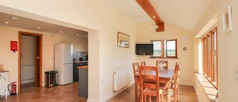 A spacious kitchen with a refrigerator, stove, and wooden cabinets. There is a dining area with a table and chairs, and a window providing natural light.