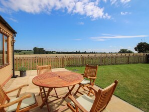 A patio with a round table and six wooden chairs, a wooden fence, and a grassy field in the background. - Ellenhall Farm Cottage (Stafford)