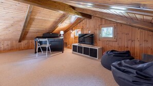A cozy attic room with a wooden sloped ceiling, a TV on a white stand, a ladder, and a bean bag. - Chalet Les Crus (Riddes)