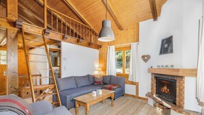 A cozy living room with a sofa, a coffee table, a fireplace, and a wooden ceiling structure. - Chalet Les Crus (Riddes)