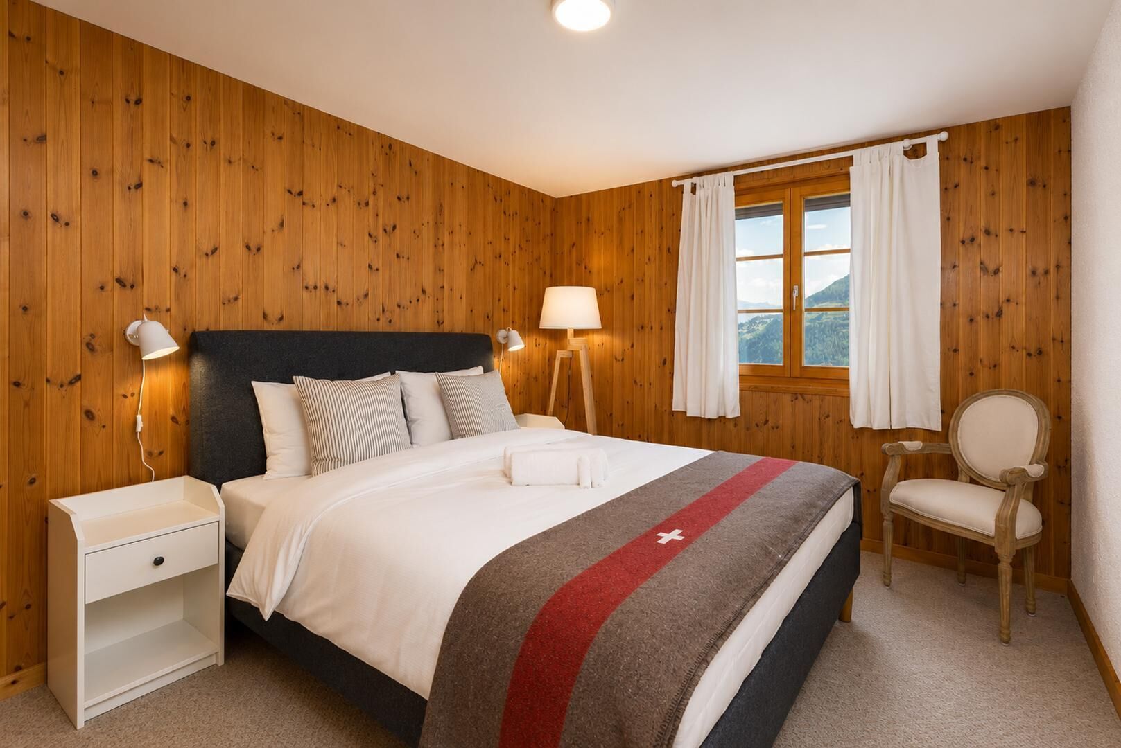 A bedroom with a bed, bedside tables, a lamp, a chair, and a window with curtains.
