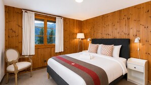 Quarto com cama, luminárias de cabeceira, uma cadeira e janela com cortinas.
