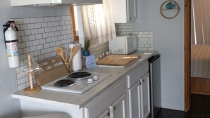 A compact kitchen with white cabinets, a stove, and a microwave. There is a welcome sign, wooden utensils, and a potted plant.