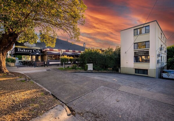 Een bakkerij-café met terras, een boom en een modern gebouw op de achtergrond.