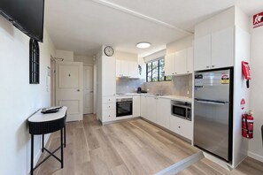 Une cuisine moderne avec des meubles blancs, un réfrigérateur en acier inoxydable et un four encastré.