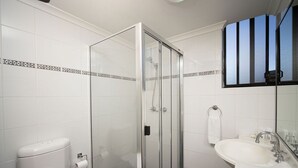 Un baño moderno con ducha envuelta en vidrio, inodoro, lavamanos y espejo.