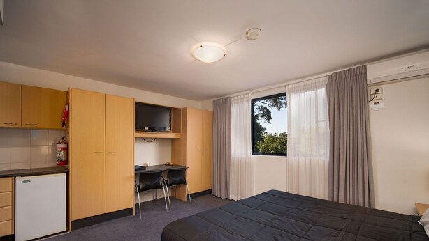 Una habitación de hotel compacta con cama, escritorio y kitchenette.