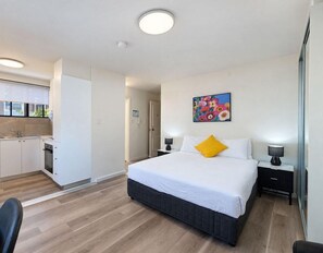 Une chambre d’hôtel moderne dotée d’un grand lit, de tables de chevet, d’un bureau et d’une kitchenette.