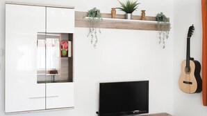 Ein modernes Wohnzimmer mit Flachbildfernseher, Holz-TV-Möbel, weißen Schränken und einer Wandmontage-Gitarre.