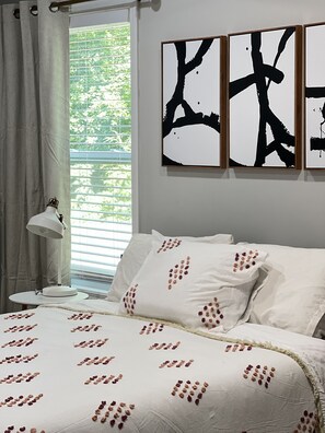 Relax in a serene bedroom with a neatly made bed, bedside table, and large window.
