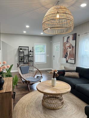 Relax in this stylish living room with a large pendant light, dark sofa, and wicker furniture.