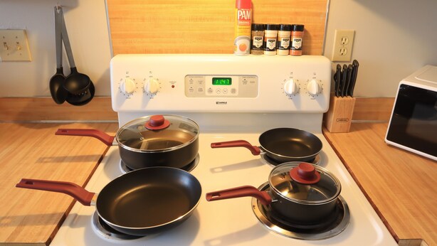 Eine Küche mit vier Töpfen auf einem Herd, einer roten PAM Spülmittelflasche und einem Gewürzregal.