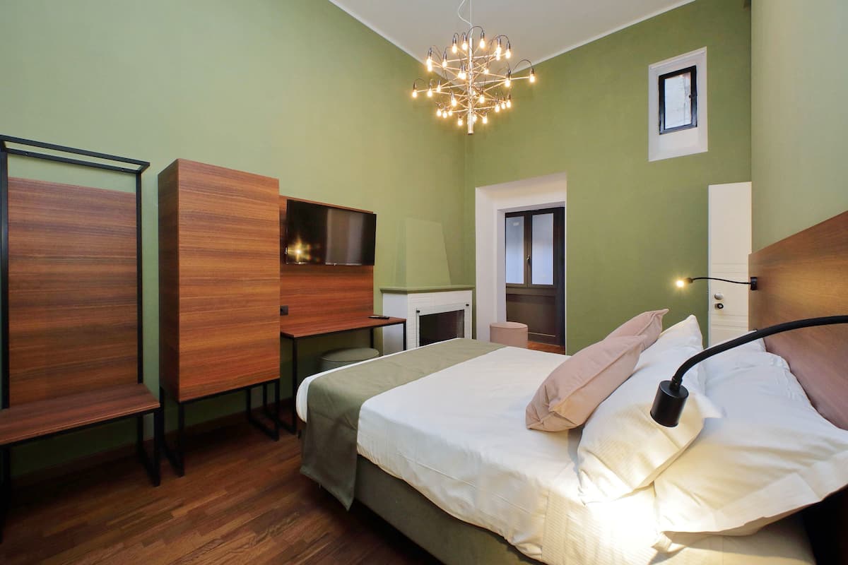 A bedroom with a bed, a desk, a chair, a wardrobe, and a small window.