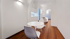 A modern interior with a long wooden table and white chairs, a kitchen area with a window, and a hallway with white walls and recessed lighting. - Youroom - Coppelle (Rome)