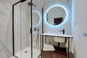 A modern bathroom with a glass shower enclosure, a wooden vanity, and a round mirror with LED lighting. - Youroom - Coppelle (Rome)