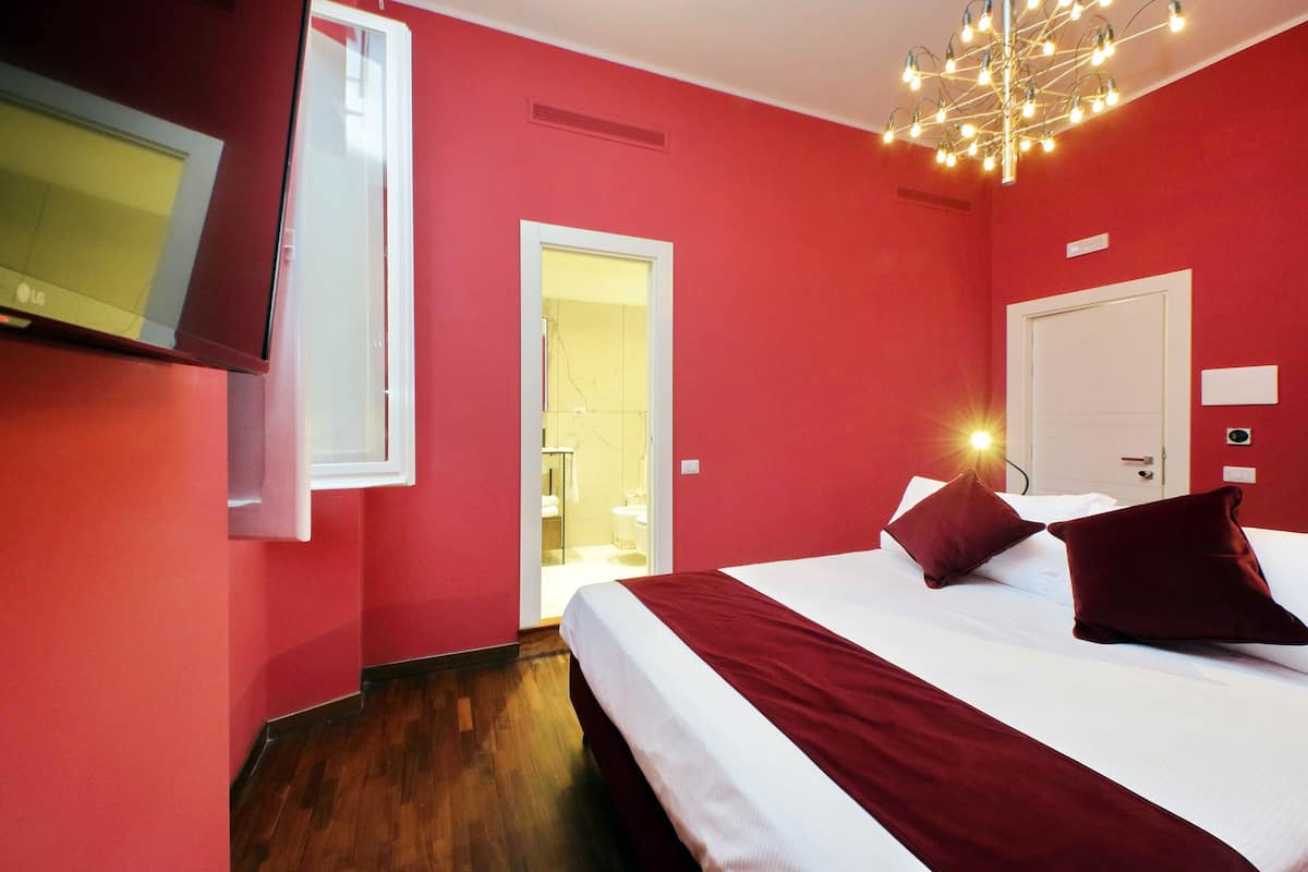 A hotel room with a bed, a TV, a door, and a light fixture.