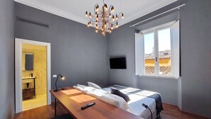 A hotel room with a wooden desk, two beds, a TV, a chandelier, and a window with a view. - Youroom - Coppelle (Rome)