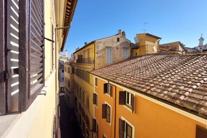 A narrow street between buildings with traditional architecture, including a yellow building with a tiled roof and shuttered windows. - Youroom - Coppelle (Rome)