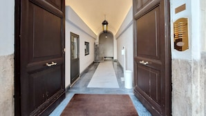 A hallway with dark wooden doors, a white marble floor, and a hanging lantern. - Youroom - Coppelle (Rome)