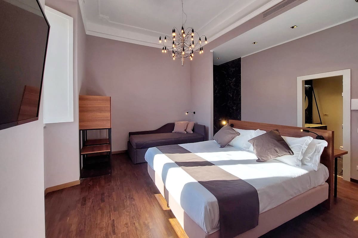 A modern bedroom with a large bed, a bedside table, a bench, and a chandelier.