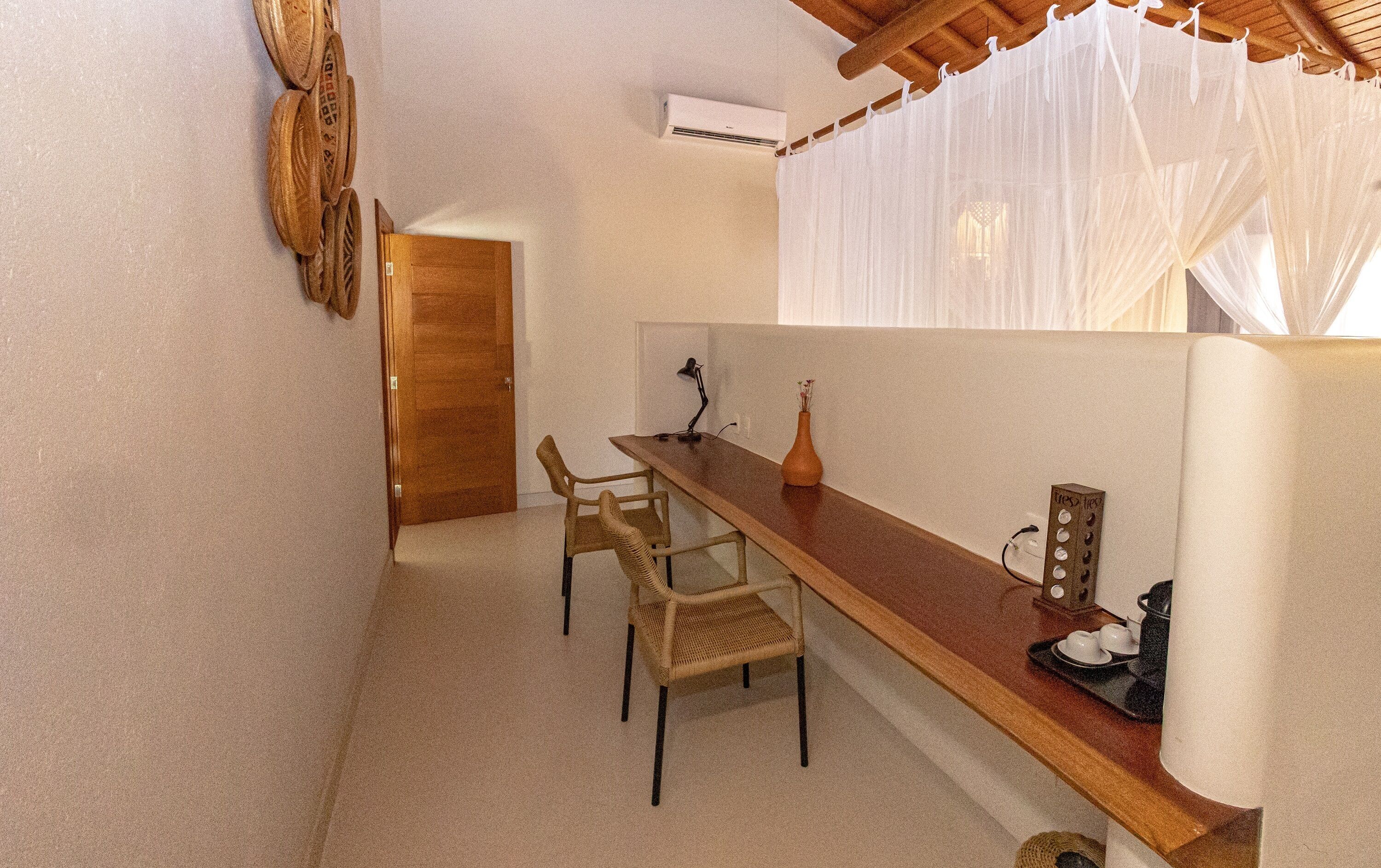 A small, cozy kitchen with a wooden table, two wicker chairs, a vase with flowers, and a coffee maker on a tray.