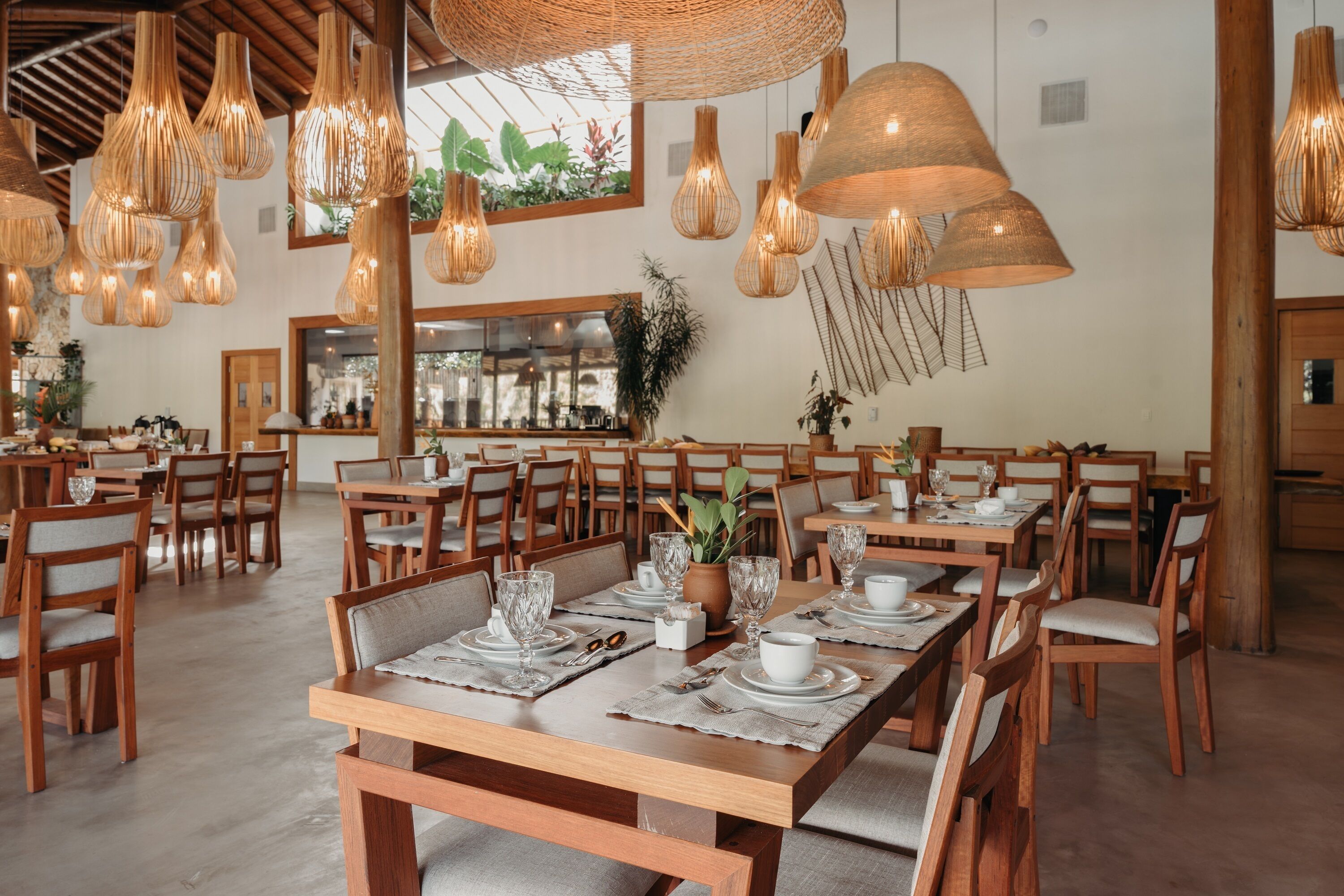 Un espace repas avec des tables et des chaises en bois, des lampes en osier suspendues et un bar en arrière-plan.