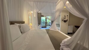 Ein Hotelzimmer mit einem großen Bett, weißen Vorhängen und Blick ins Freie.