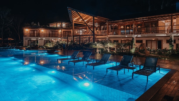 Ein Poolbereich bei Nacht mit Liegestühlen und einem Gebäude mit mehreren Balkonen.