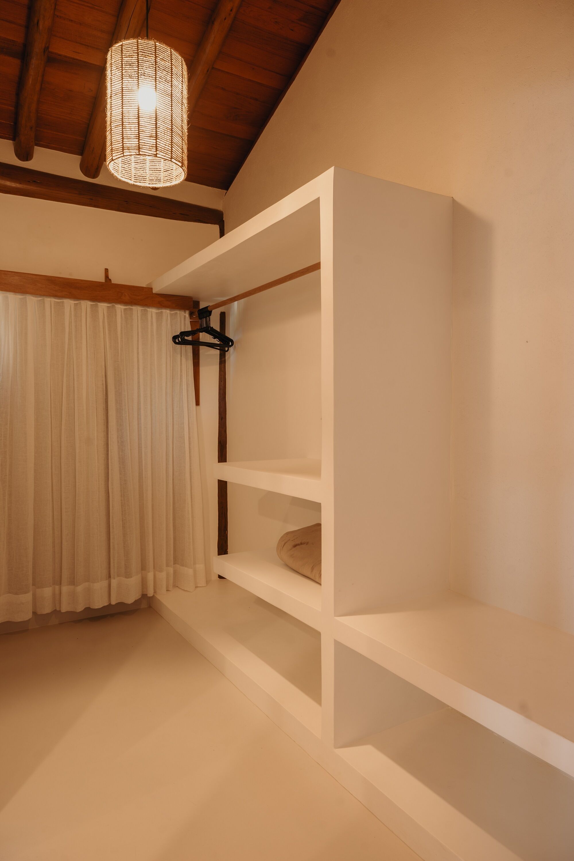 Una habitación con techo de madera, lámpara colgante, pared blanca y cortina blanca.