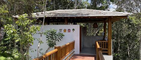 A wooden bridge leading to a covered area with a tiled roof, surrounded by lush greenery.