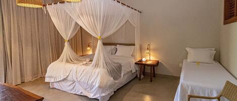 A bedroom with a four-poster bed, a bedside table with a lamp, and a single bed with a chair.